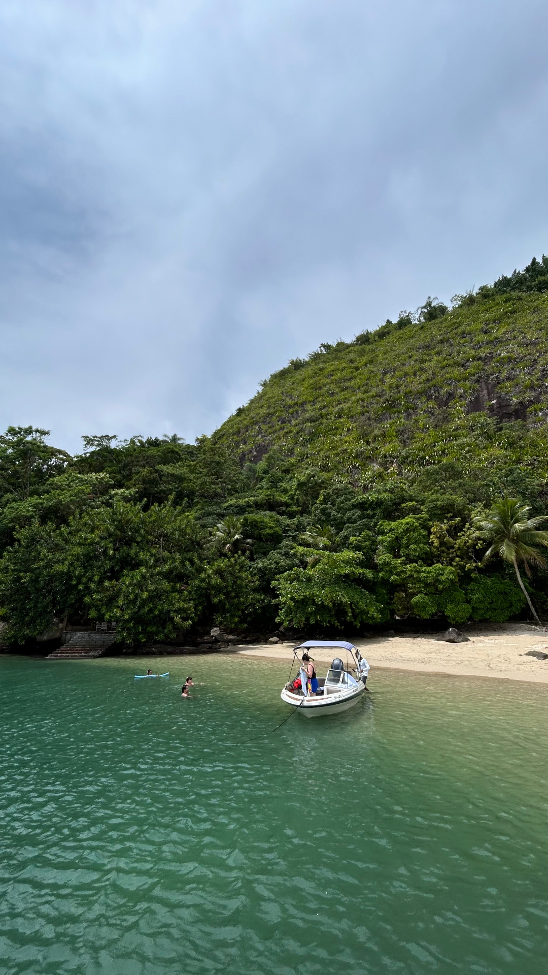 Barco ancorado em enseada de água verde com praia deserta