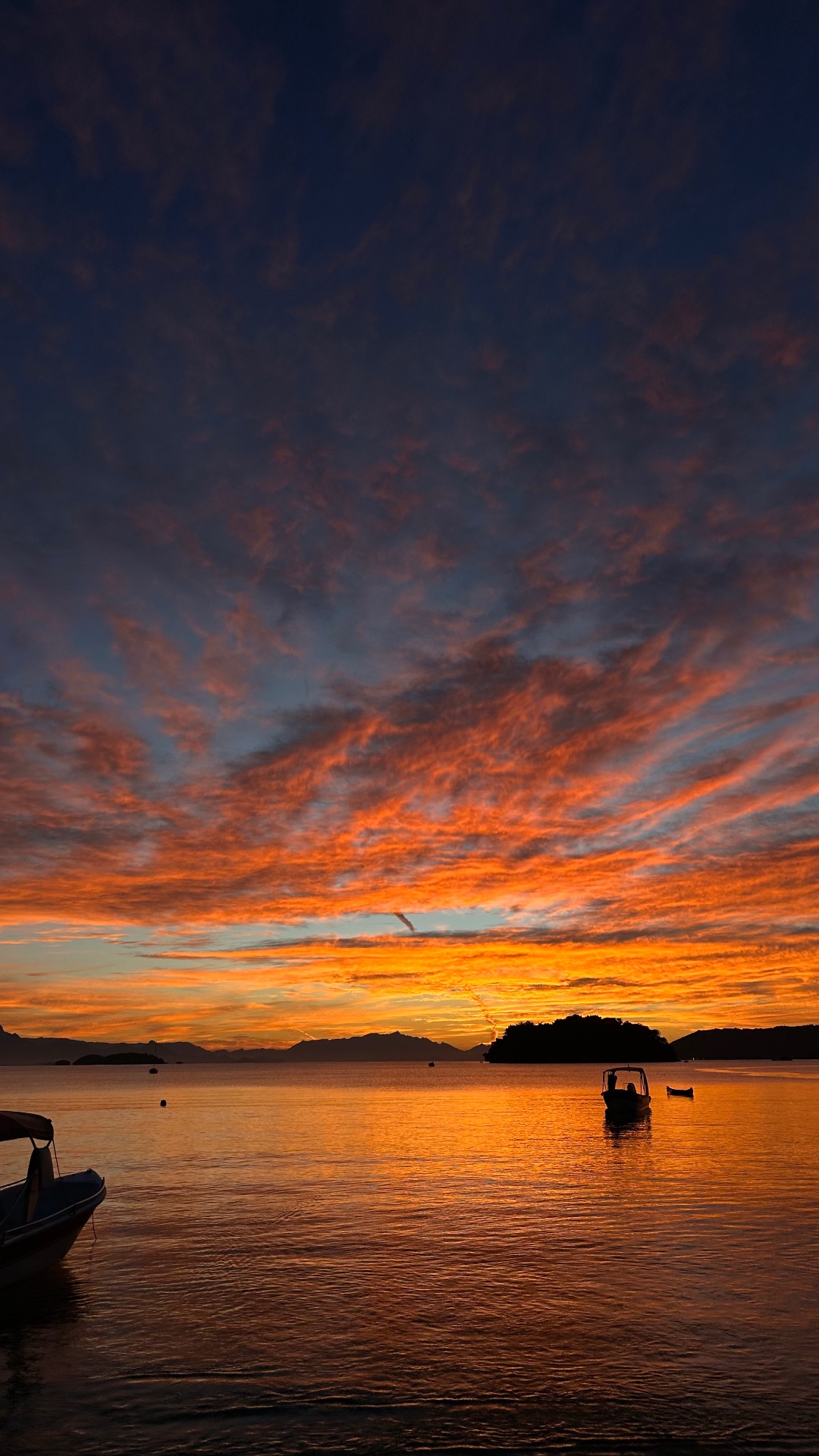 Pôr do sol alaranjado sobre a baía de Paraty com barcos ancorados